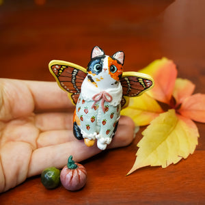 Calico cat with butterfly wings and strawberry sweater