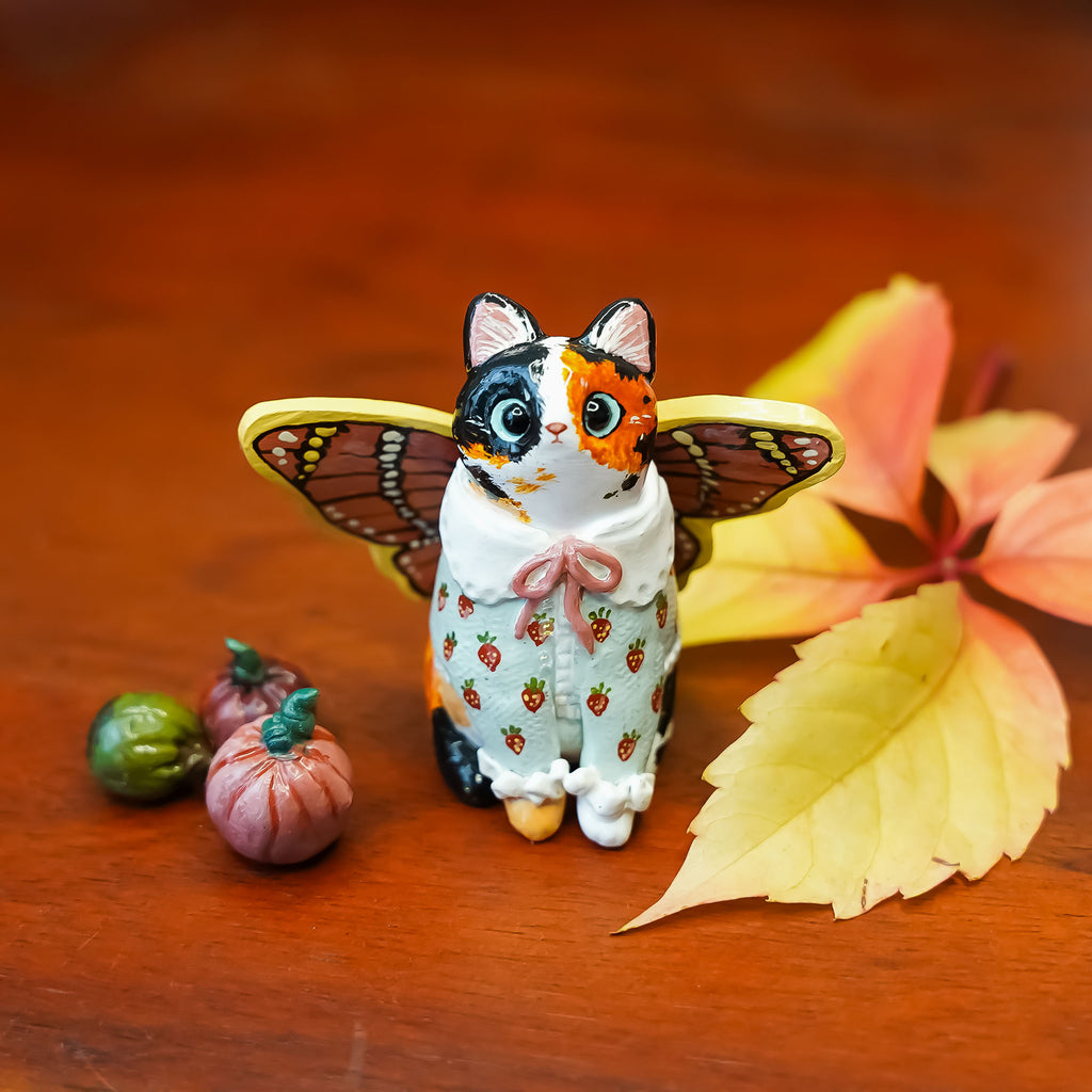 Calico cat with butterfly wings and strawberry sweater